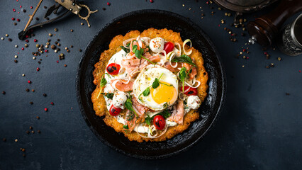 Large potato pancake with salmon fish, tomatoes, egg, onion, herbs and sour cream in a frying pan.
