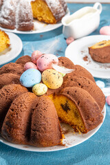 Traditional cake for Easter. Chocolate and vanilla Easter round cake with chocolate and sugar powder sprinkles, colorful Easter eggs, spring flowers, on a blue background copy space