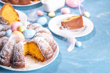 Traditional cake for Easter. Chocolate and vanilla Easter round cake with chocolate and sugar powder sprinkles, colorful Easter eggs, spring flowers, on a blue background copy space