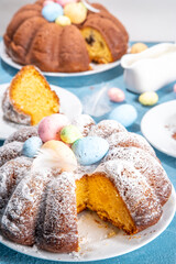 Traditional cake for Easter. Chocolate and vanilla Easter round cake with chocolate and sugar powder sprinkles, colorful Easter eggs, spring flowers, on a blue background copy space