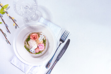 Easter table setting. Festive spring holiday cutlery set, with plate, wine glass, knife, fork, with Easter decor egg nest, willow flower branches, white sunny table background copy space top view