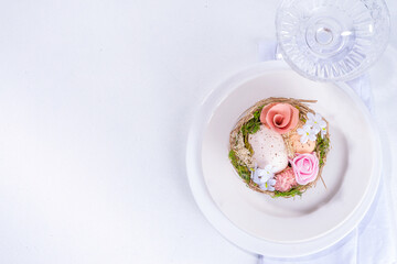 Easter table setting. Festive spring holiday cutlery set, with plate, wine glass, knife, fork, with Easter decor egg nest, willow flower branches, white sunny table background copy space top view