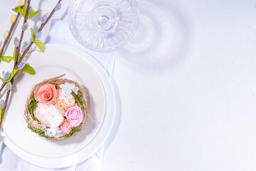Easter table setting. Festive spring holiday cutlery set, with plate, wine glass, knife, fork, with Easter decor egg nest, willow flower branches, white sunny table background copy space top view