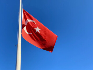 Red turkish flag on the blue sky background, half-mast flag as a mourning symbol