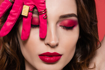 close up of woman in magenta color glove with golden rings covering closed eye isolated on pink.