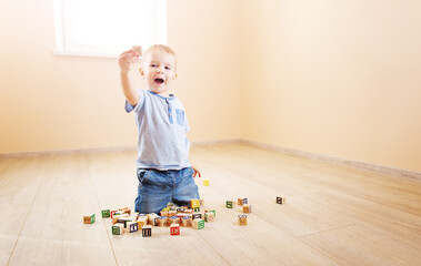 Little boy sitting on the floor indoor and playing with wooden cubes.