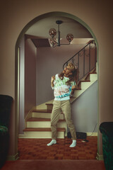 vintage lifestyle portrait of a young blonde woman in a late 80s, early 90s, interior decor, singing to music playing on a tape recorder in front of a staircase