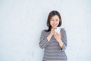 明るいリビングでスマートフォンを操作する笑顔の30代女性一人