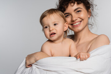 smiling mother and toddler baby girl covered in duvet isolated on grey.