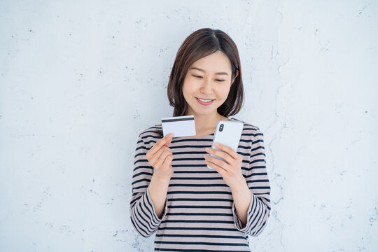 明るいリビングでスマートフォンとクレジットカードを持つ笑顔の30代女性一人