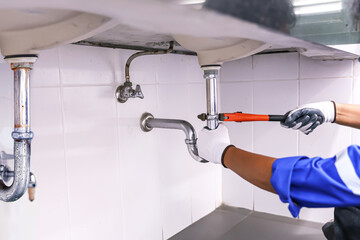 Technician plumber using a wrench to repair a water pipe under the sink. Concept of maintenance, fix water plumbing leaks, replace the kitchen sink drain, cleaning clogged pipes is dirty or rusty.