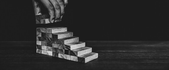 Hand placing wooden block tower stack in pyramid stair step with caution to prevent collapse or...