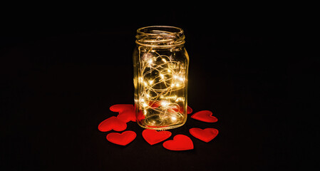 A magical glow in the glass. Red hearts on black fabric. View from above..