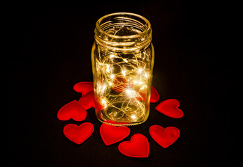 Atmospheric photo of glowing red hearts in glass. Black background.
