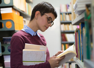 Young smiling woman student reading books and studying in the library