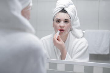young brunette paints her lips with red lipstick, looking in the mirror