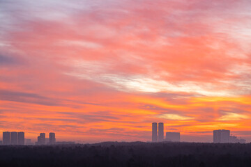 Fototapeta na wymiar red and orange sky over city park and towers at cold dawn