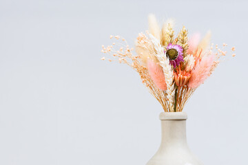 bouquet of dried flowers and spikelets in neck of ceramic bottle on gray background with copyspace