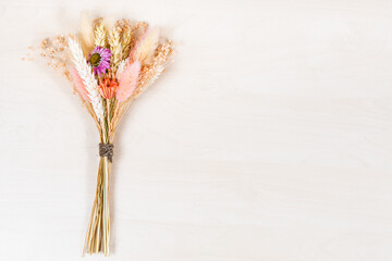 top view of tied bouquet of dried flowers and spikelets lies on light brown wooden background with...