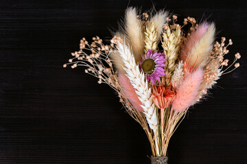 tied bouquet of dried flowers and spikelets lies on dark wooden board with copyspace
