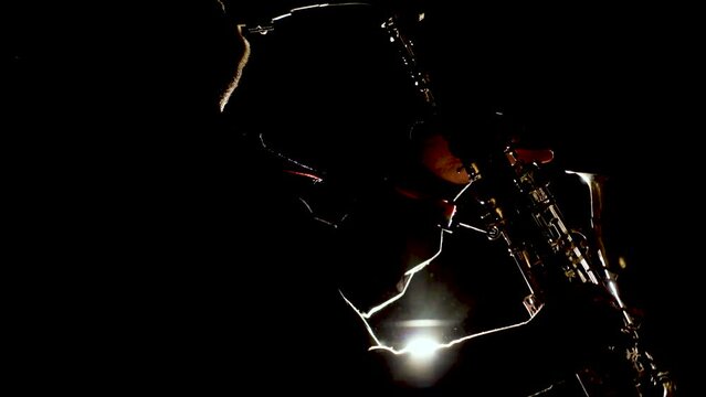 a man blows a saxophone against the light. Contours of the body, contours of the tool