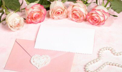 Festive mock up with pink roses, envelope with lace heart, empty white sheet, pearl beads on pink.