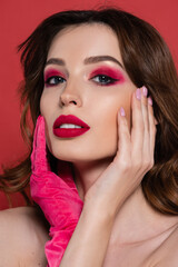 portrait of young woman with magenta color glove looking at camera while touching face isolated on pink.