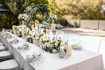 A general plan of a wedding decor from an arch decorated with fresh white flowers and a festive table for guests with a serving decorated with white flowers and various candles