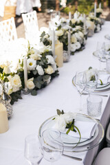 Wedding decorations. Served wedding table with decorative fresh white flowers and candles. Celebration details. flower composition roses plates and candles in candlesticks