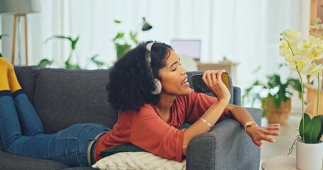 Headphones, phone and black woman dance on sofa in home living room streaming music, radio or...