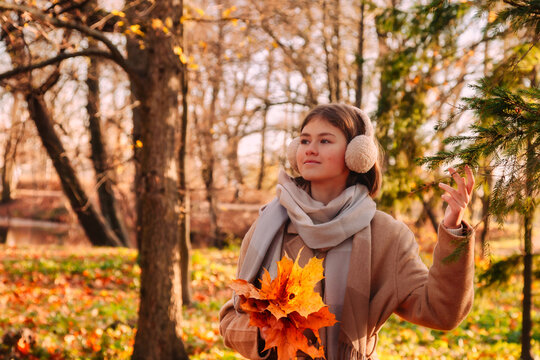 Portrait stylish teen girl model in beige coat walking in fall park on sunset outdoor. Smiling cute young lady with autumn leaves leisure. Fashion youth style concept. Copy text space for advertising