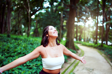 Brazilian young woman happy smiling with open arms in a park in the shade of the trees