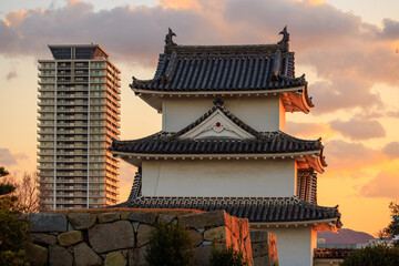 Fototapeta na wymiar Sunset over watchtower in Japanese castle and modern high rise apartment building