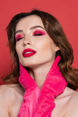 portrait of young woman with magenta color eye shadow touching neck isolated on pink.