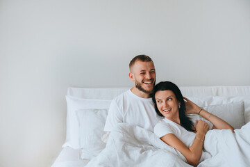 Laughing young couple awakening at new apartment happy smiling laying on bed at empty wall. Handsome beardy man excited to be owner of house. Succesful people. Newlyweds enjoying vacations at hotel.