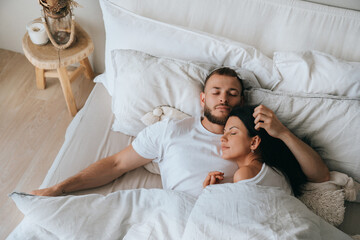 Young caucasian sleeping couple in bed. Handsome beardy European man laying with wife at bedroom enjoying Sunday morning. Calm hispanic young adult woman having nap at hotel with husband. - Powered by Adobe