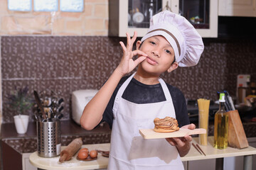 Cheerful little chef showing good taste while holding baked bread in the kitchen 