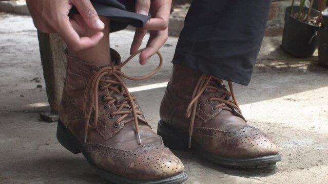 a man is taking off old brown leather shoes while sitting