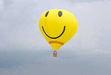 Yellow balloon with the smiley face symbol on it flying in the cloudy sky