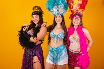 three brazilian female friends with queen clothes from samba school, carnival. Feather crown.