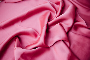 A folded pink silk fabric lies in folds on the table. Drapery texture. Synthetics Atlas