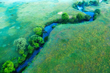 The channel and bends of the river, on a marshy meadow. Orange dry grass, scorched by the summer heat, and morning fog. A wonderful landscape at dawn. Drone view.