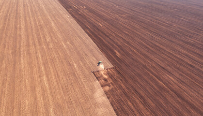 A tractor in the field cultivates the soil before the start of the sowing campaign. Drone view.