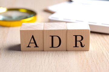 ADR on wooden cubes with magnifier and calculator, financial concept background