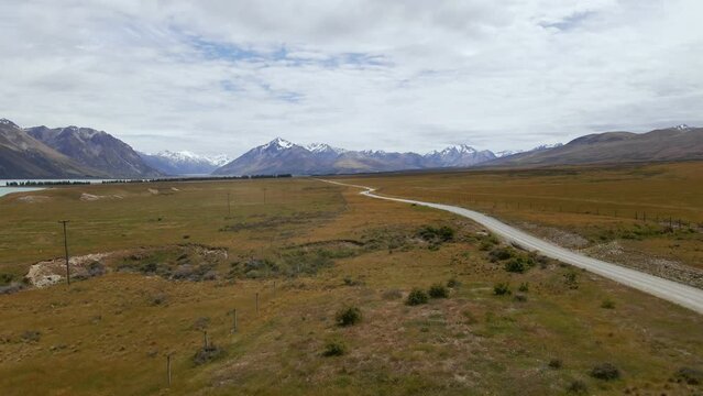 Dusty dirt road within dry plains leading towards stunning snow covered mountains