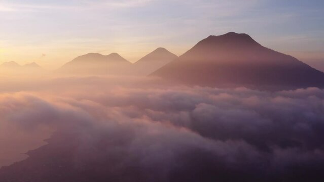 Epic sunrise drone flight at cloud level over San Pedro la Laguna around Atitlan Lake in Guatemala, with three volcanos visible in shot.