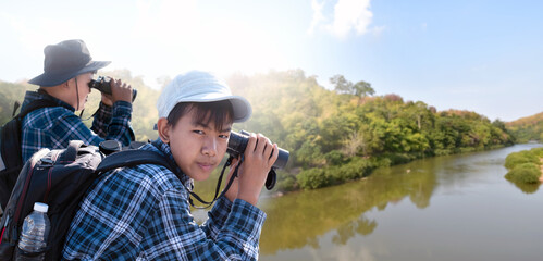 Obraz premium Asian boys are using binoculars to do the birdwatching in tropical forest during summer camp, idea for learning creatures and wildlife animals and insects outside the classroom.