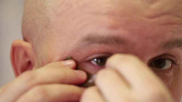 a man sticks cosmetic patches under his eyes while standing in the bathroom