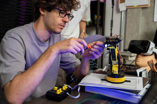 Modern male engineer and expert in programming and manipulation of robotic arm motion, modern facility, couple helping repair robotic arm and programming together in conference room.