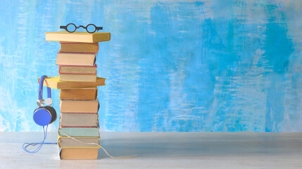 audio book concept with large stack of books spectacles and vintage headphones,blue paint background